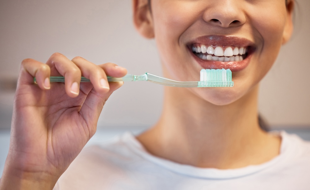 A close up of a female patient's lower face, her hand is holding a toothbrush, ready for dental cleaning near Waxhaw.