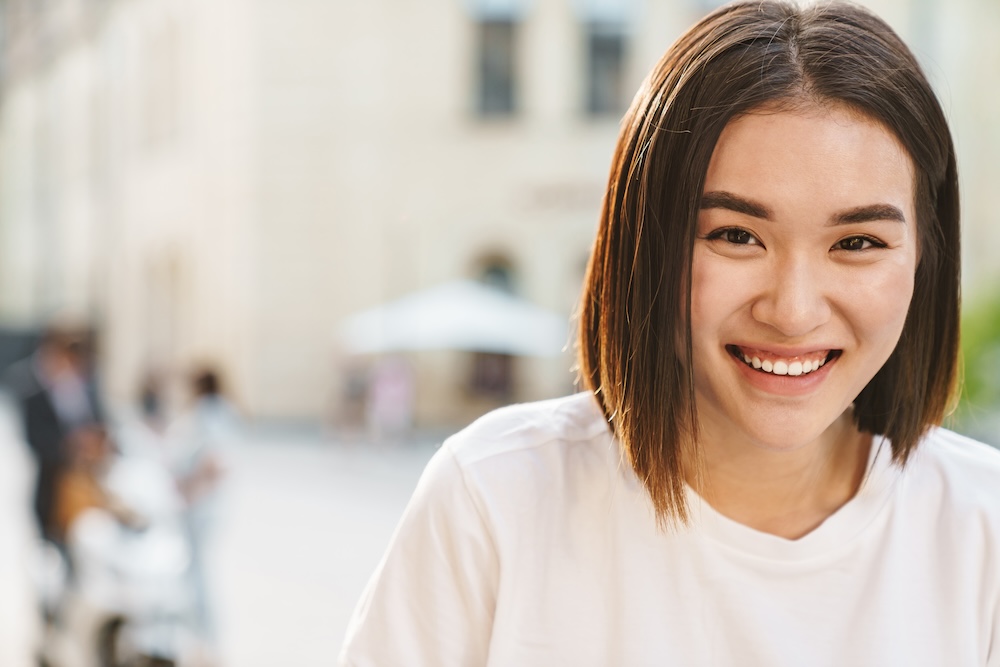Close up of a smiling young Asian woman standing in a street wearing her clear aligners in Waxhaw.