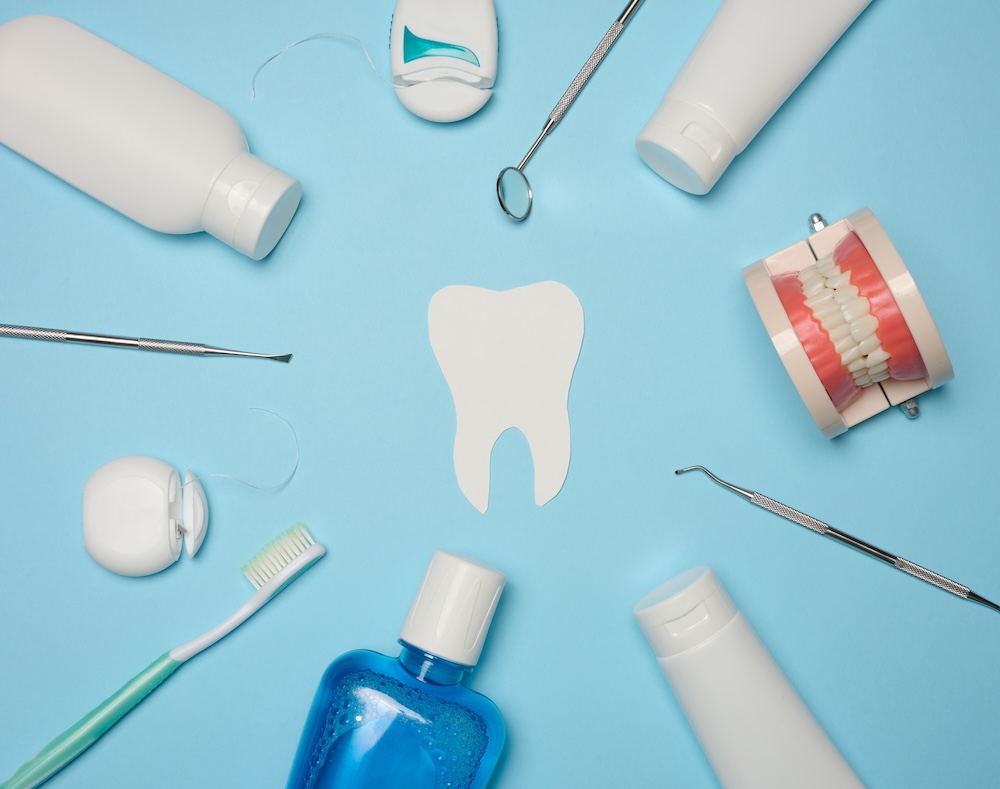 Flat lay of dental supplies on a sky blue background spaced in a circle around a white tooth cut-out. We use these supplies for professional teeth cleaning in Waxhaw.