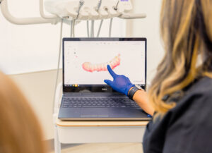 A female Dogwood Dental Spa provider, wearing black scrubs and blue gloves, shows a female patient her digital dental impression. These impressions are sent to a special lab to create dental crowns near Waxhaw.
