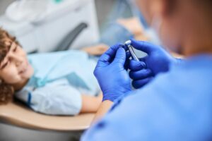 A female Dogwood Dental Spa provider shows a child patient, reclining in a treatment chair, a metal tool used to clean teeth. Regular teeth cleaning and dental sealant in Waxhaw can prevent tooth damage and decay.